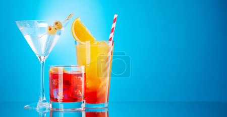 Foto de Cócteles Negroni, tequila sunrise y martini sobre fondo azul con espacio para copiar - Imagen libre de derechos