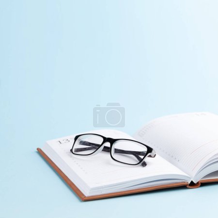 Téléchargez les photos : Bloc-notes et lunettes sur fond bleu avec espace de copie - en image libre de droit