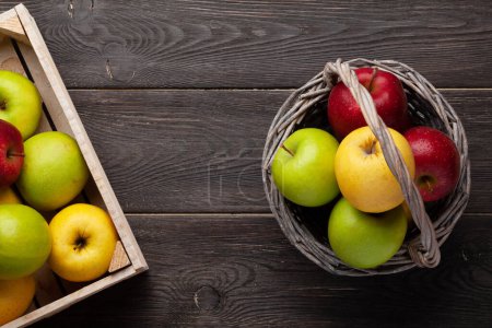 Foto de Coloridos frutos maduros de manzana en cesta y caja sobre mesa de madera. Vista superior plano con espacio de copia - Imagen libre de derechos