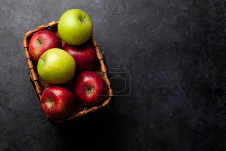 Foto de Coloridos frutos maduros de manzana en canasta sobre una mesa de piedra. Vista superior plano con espacio de copia - Imagen libre de derechos