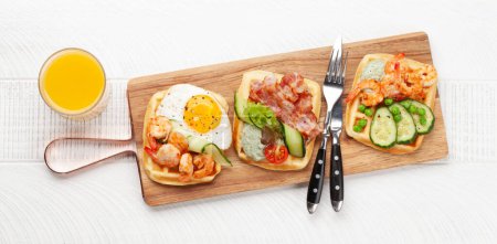 Foto de Desayuno gofres con huevos fritos, salmón, tocino, pepino y gambas. Vista superior plano con espacio de copia - Imagen libre de derechos