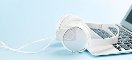 Foto de Auriculares blancos y portátil sobre fondo azul con espacio de copia. Podcast, audiolibro o plantilla de música - Imagen libre de derechos