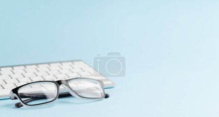 Photo for Pc keyboard and glasses on blue background with copy space - Royalty Free Image