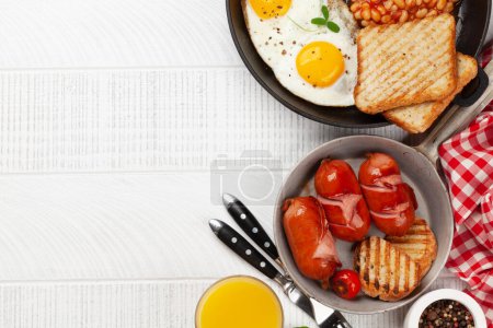 Foto de Desayuno inglés con huevos fritos, frijoles, tocino y salchichas. Café y jugo de naranja. Vista superior plano con espacio de copia - Imagen libre de derechos