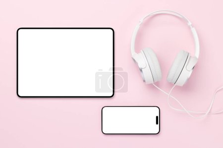 Téléchargez les photos : Casques, tablette et smartphone avec écran blanc sur fond rose. Pose plate avec espace de copie - en image libre de droit