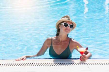 Photo for Woman with heart shaped sunglasses relaxing at the swimming pool with tropical cocktail. With copy space - Royalty Free Image