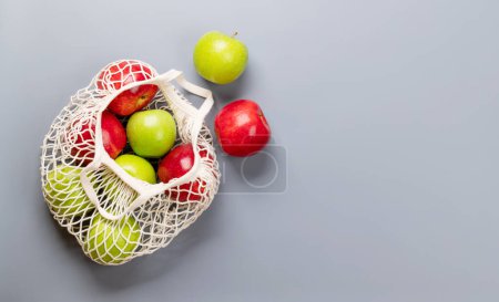 Téléchargez les photos : Pommes rouges et vertes dans un sac en filet sur fond gris. Pose plate avec espace de copie - en image libre de droit