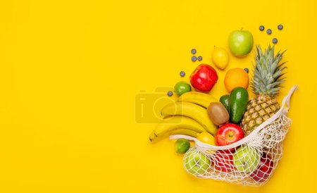 Foto de Bolsa de malla de compras llena de alimentos frutas saludables sobre fondo amarillo. Piso con espacio de copia - Imagen libre de derechos