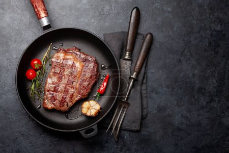 Téléchargez les photos : Steak de bœuf côtelé grillé dans une poêle avec des herbes et des épices. Pose plate avec espace de copie - en image libre de droit