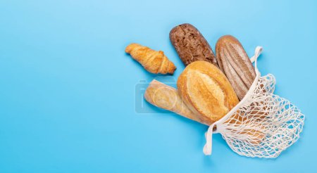 Photo for Fresh baked bread in mesh bag on blue background. Flat lay with copy space - Royalty Free Image