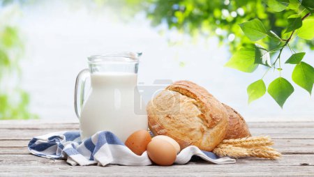 Photo for Homemade bread and milk in pitcher on wooden table. Outdoor - Royalty Free Image