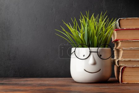 Photo for Old books and potted plant with glasses on wooden table and blackboard for copy space. School and education template - Royalty Free Image
