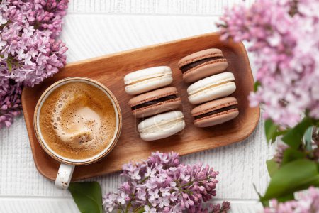 Foto de Galletas macarrones y café. Sobre mesa de madera con flores lila. Vista superior plano laico - Imagen libre de derechos