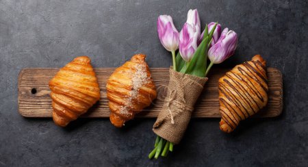 Foto de Varios croissants en tabla de madera y ramo de tulipanes. Desayuno francés. Vista superior plano laico - Imagen libre de derechos