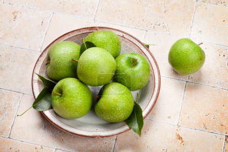 Foto de Manzanas verdes frescas en plato sobre mesa de piedra - Imagen libre de derechos
