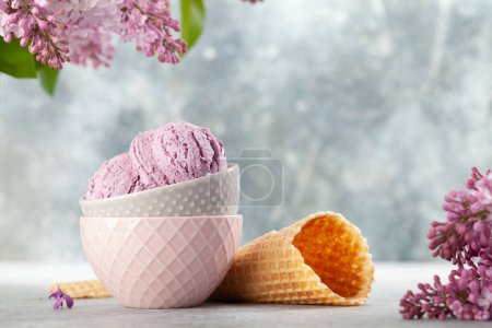 Foto de Helado de helado en cuenco, conos de gofre y flores lila - Imagen libre de derechos