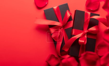 Téléchargez les photos : Carte Saint Valentin avec coffrets cadeaux et pétales de fleurs de rose. Sur fond rouge avec espace pour vos salutations - en image libre de droit