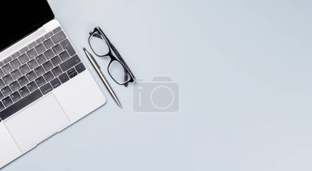 Foto de Escritorio de oficina de vista superior con laptop, artículos de oficina y anteojos. Espacio de trabajo plano con luz soleada y espacio de copia - Imagen libre de derechos