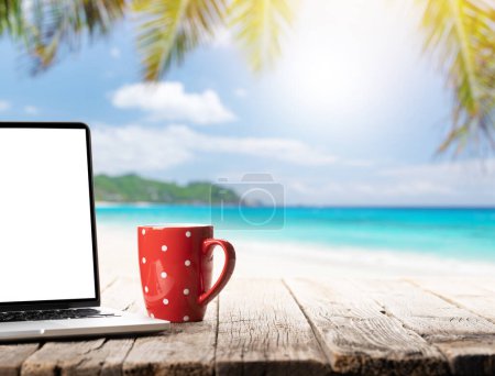 Photo for Laptop and coffee cup on wooden table in front of sunny sea and palm leaves. Work and travel or remote business concept - Royalty Free Image