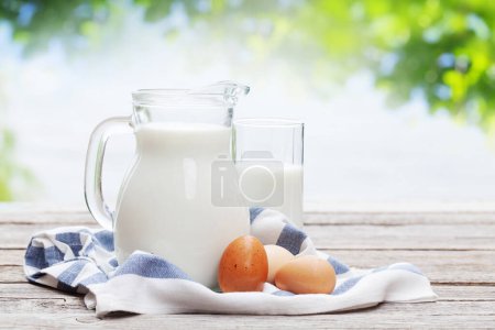 Photo for Milk in pitcher and glass on garden wooden table. Outdoor - Royalty Free Image
