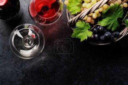 Copas de vino, botellas y uvas en cesta. Piso con espacio de copia