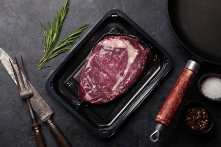 Téléchargez les photos : Steak de bœuf emballé sous vide. Ribeye steak et ustensiles de cuisine. Vue du dessus plat lay - en image libre de droit