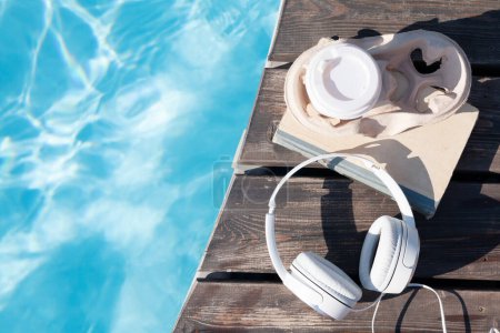 Foto de Libro y auriculares cerca de la piscina. Vacaciones de verano. Piso con espacio de copia - Imagen libre de derechos