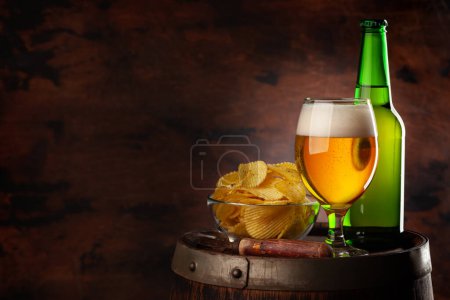 Téléchargez les photos : Verre à bière, bouteille et croustilles sur tonneau en bois. Avec espace de copie - en image libre de droit