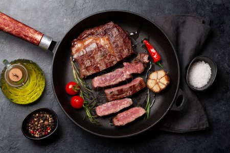 Photo for Grilled ribeye beef steak in frying pan with herbs and spices. Flat lay - Royalty Free Image