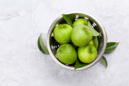 Foto de Manzanas verdes frescas en colador sobre mesa de piedra. Piso con espacio de copia - Imagen libre de derechos