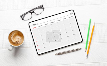 Foto de Tableta con aplicación de calendario, taza de café y suministros de oficina en el escritorio. Vista superior plano laico - Imagen libre de derechos
