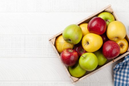 Foto de Coloridos frutos maduros de manzana en caja sobre mesa de madera. Vista superior plano con espacio de copia - Imagen libre de derechos