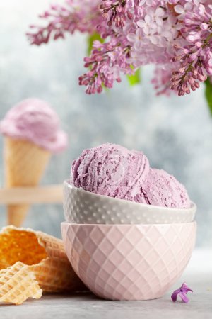 Foto de Helado de helado en cuenco, conos de gofre y flores lila - Imagen libre de derechos