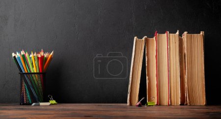 Photo for Old books and colorful pencils on wooden table and blackboard for copy space. School and education template - Royalty Free Image