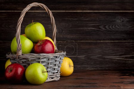 Foto de Coloridos frutos maduros de manzana en cesta sobre mesa de madera. Con espacio de copia - Imagen libre de derechos