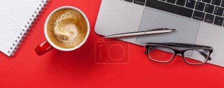 Téléchargez les photos : Bureau en toile de fond rouge avec tasse à café, fournitures et ordinateur. Pose plate. - en image libre de droit