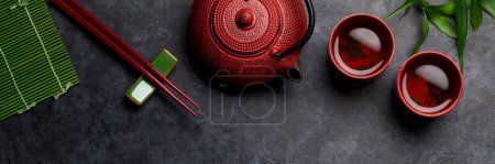 Téléchargez les photos : Thé vert dans des bols et des baguettes de théière et de sushi sur une table en pierre. Vue du dessus plat lay - en image libre de droit