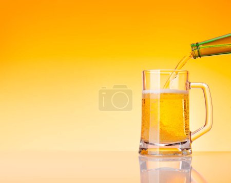 Foto de Cerveza que vierte de la botella en el vidrio delante del fondo amarillo. Estudio con espacio de copia - Imagen libre de derechos