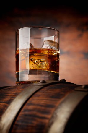 Foto de Un vaso de whisky con cubitos de hielo en el viejo barril. Con espacio de copia sobre fondo de madera - Imagen libre de derechos
