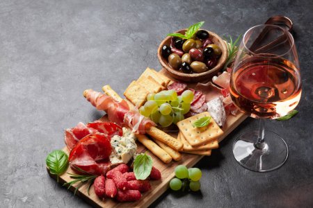 Photo for Antipasto board with prosciutto, salami, crackers, cheese, nuts, olives and rose wine. With copy space - Royalty Free Image
