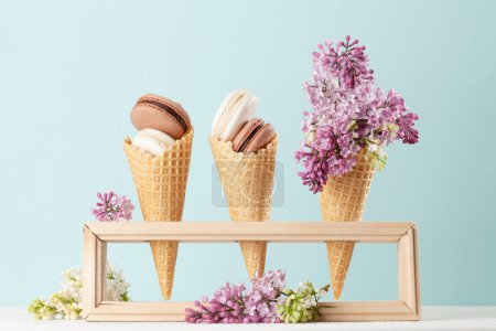 Photo for Various macaroon cookies in ice cream cones and lilac flowers - Royalty Free Image