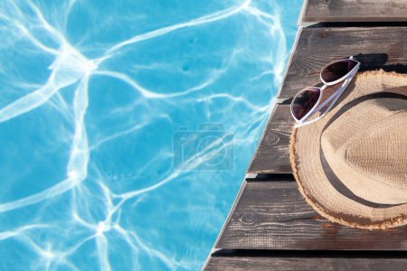 Téléchargez les photos : Lunettes de soleil et chapeau près de la piscine. Vacances d'été. Pose plate avec espace de copie - en image libre de droit