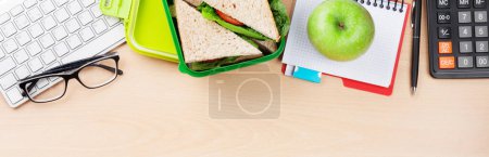 Téléchargez les photos : Bureau avec fournitures et boîte à lunch avec légumes et sandwich. Vue du dessus plat lay - en image libre de droit