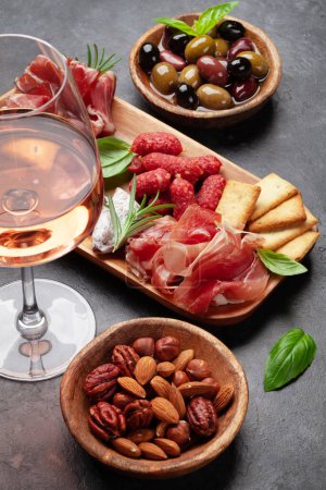 Photo for Antipasto board with prosciutto, salami, crackers, cheese, nuts, olives and rose wine - Royalty Free Image