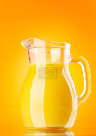 Photo for Fresh orange juice in a glass pitcher over orange background - Royalty Free Image