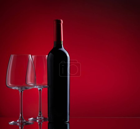 Téléchargez les photos : Verres à vin rouge et bouteille sur fond rouge avec espace de copie - en image libre de droit