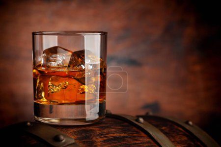 Un vaso de whisky con cubitos de hielo en el viejo barril. Con espacio de copia sobre fondo de madera