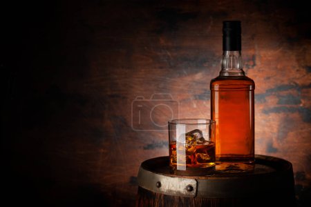 Foto de Un vaso de whisky con cubitos de hielo y una botella en el barril viejo. Con espacio de copia sobre fondo de madera - Imagen libre de derechos