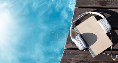 Foto de Libro y auriculares cerca de la piscina. Vacaciones de verano. Piso con espacio de copia - Imagen libre de derechos