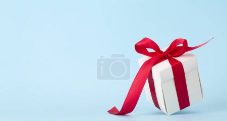 Photo for White gift box with red ribbon over blue background. With space for your Christmas, birthday or Valentines day greetings - Royalty Free Image